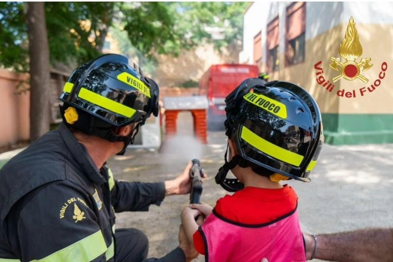 Un bambino impegnato nel percorso ludico della pompieropoli aiutato da un vigil del fuoco